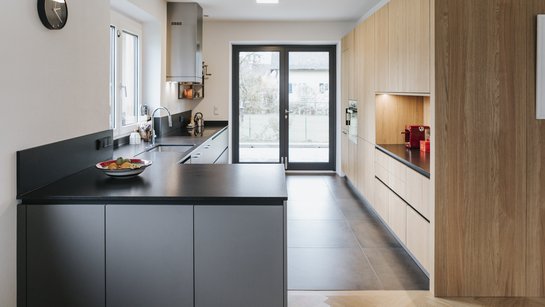 Küche bestehend aus einer grauen und einer Holz-Küchenzeile in länglichem Raum