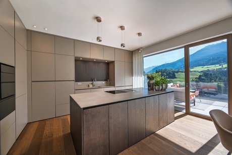 Kücheninsel mit hochgestellt integrierten Elektrogeräten und deckenhohen Hochschränken in fango