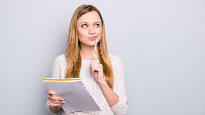 Eine junge blonde Frau hat einen Block und einen Stift in der Hand und überlegt intensiv.
