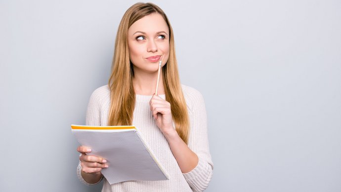 Eine junge blonde Frau hat einen Block und einen Stift in der Hand und überlegt intensiv.