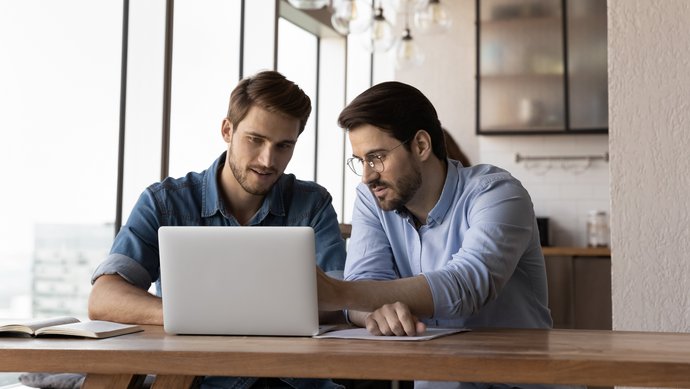 Zwei junge Männer sitzen an einem Tisch vor einem Laptop