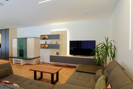 Wohnzimmer mit grauer Couch, an der Wand ein Sideboard und hängende längliche Regale mit grauen Fronten