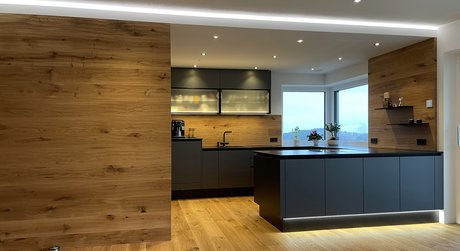 Dunkelgraue Inselküche mit Holzrückwand und Glasoberschränken