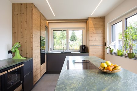 ewe nanoo®/Sintesa in carbon metallic/kiefer antik | Laserer Tischlerei Inselküche mit Arbeitsplatte aus grünem Stein, Küchenfronten in dunkelgrau und kiefer