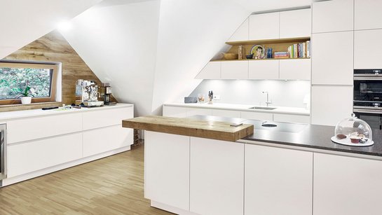 Weiße Küche mit Thekenplatte aus Holz, die perfekt an einen Raum mit Dachschräge angepasst wurde