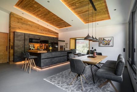 Inselküche in Betonoptik im Industrial Style mit Holzumrahmung, davor ein Esstisch mit Stühlen
