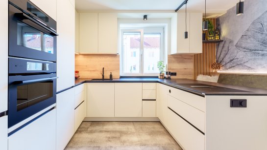 Gesamtansicht der Küche mit Hochschränken, hochgestellten Elektrogeräten und flächenbündiger Spüle.